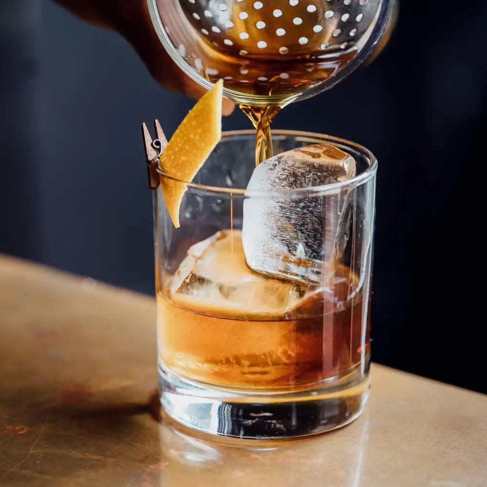 An Old Fashioned strained over one big ice cube, orange peel clipped to the glass