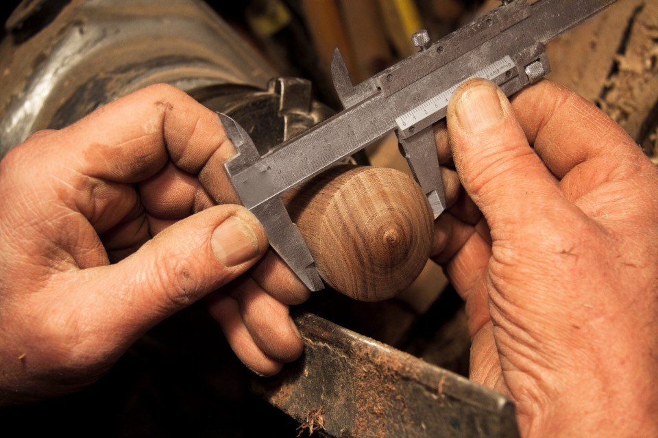 A woodworker's hands measuring a turned wooden knob with steel calipers