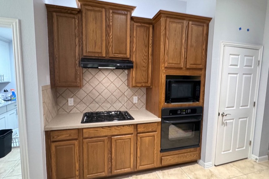 Existing kitchen: orange oak cabinets, a diagonal beige tile backsplash, a black range hood and a stacked black microwave and wall oven