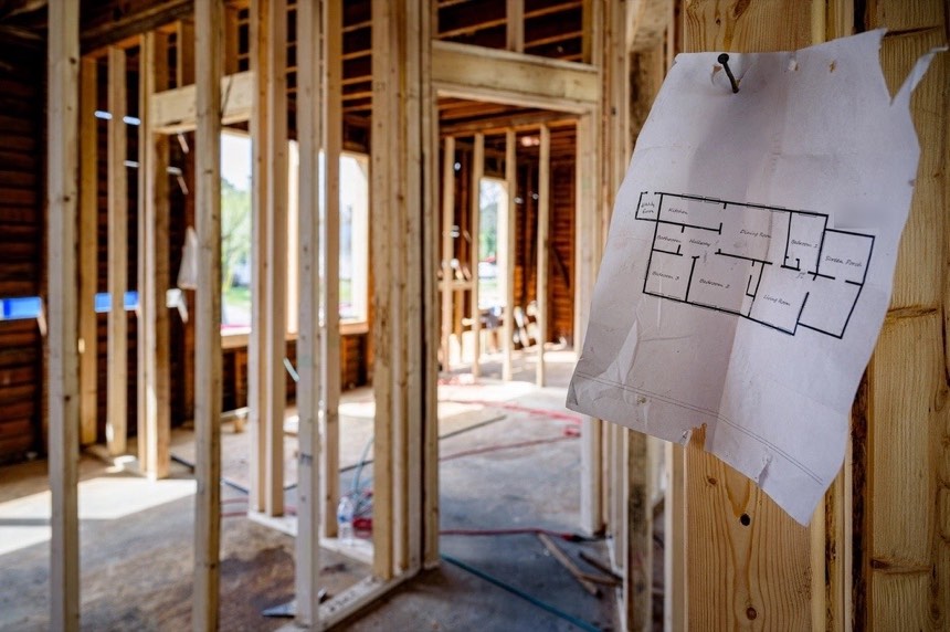 New wall framing inside a house under renovation, with a printed floor plan nailed to a stud
