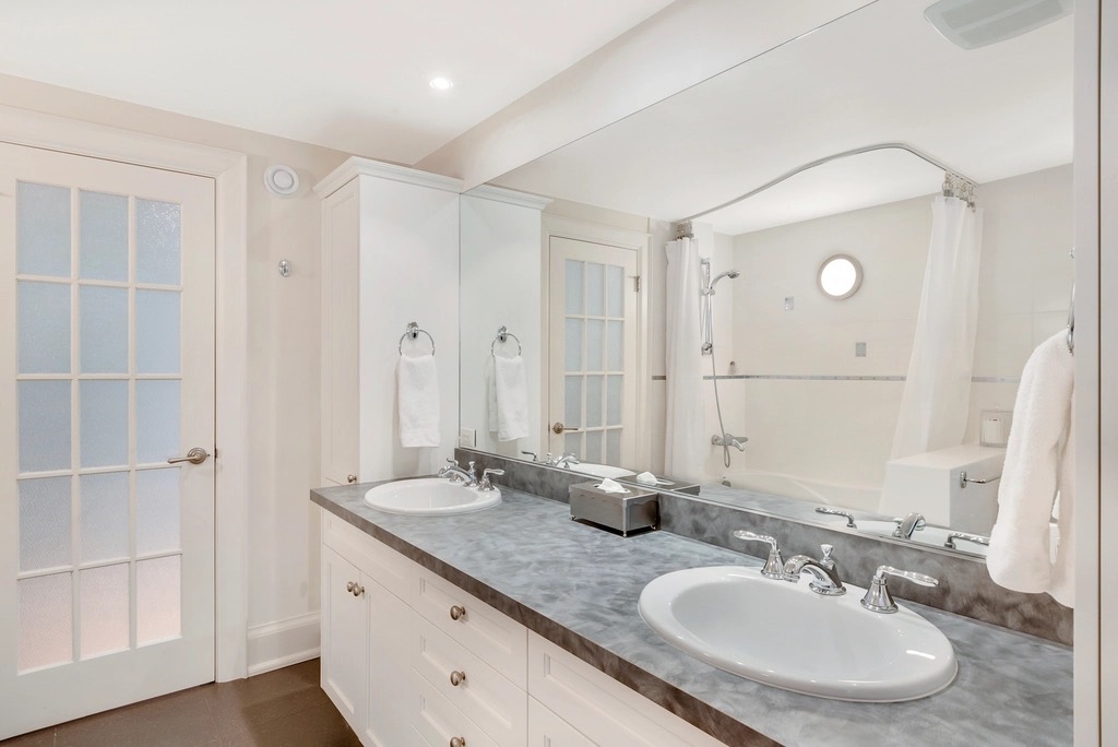 A white bathroom with a long vanity, two sinks and a large mirror, all wiped and shining