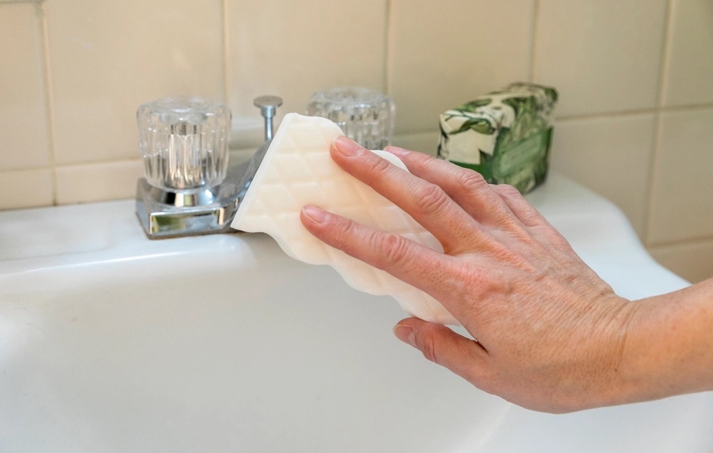 Marisol scrubbing a bathroom sink by hand beside the faucet