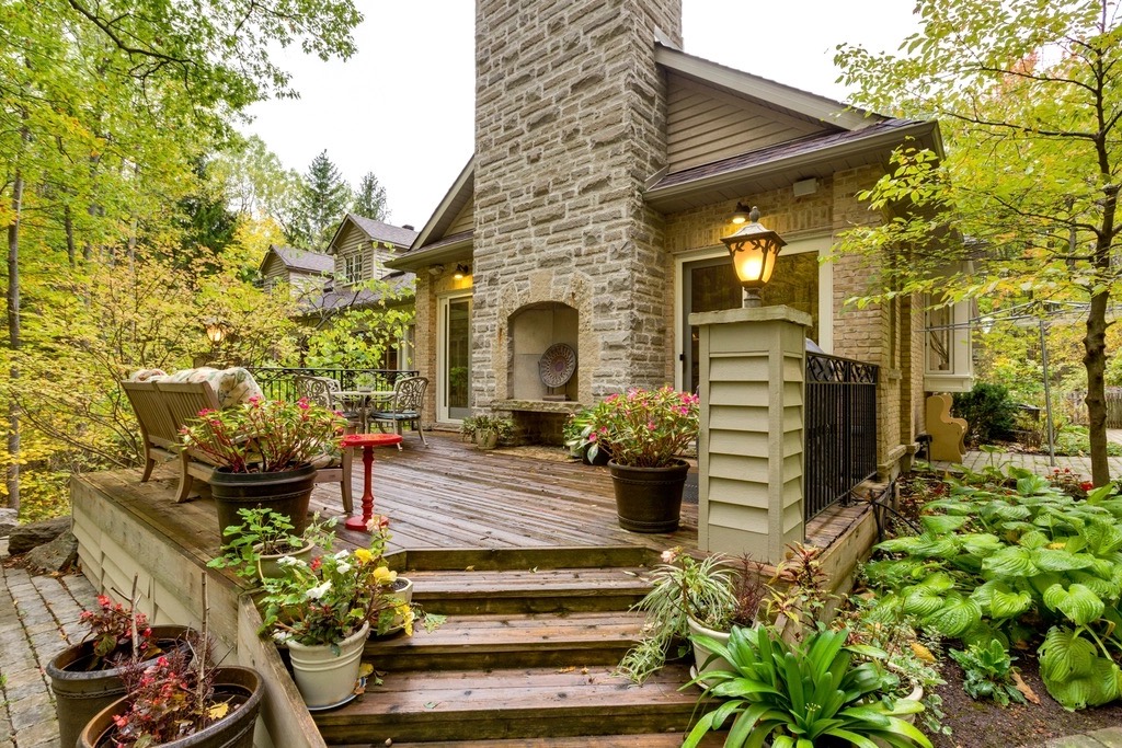 Wooden deck and wide steps beside a stone chimney, edged with pots and a bed of large-leaved hostas