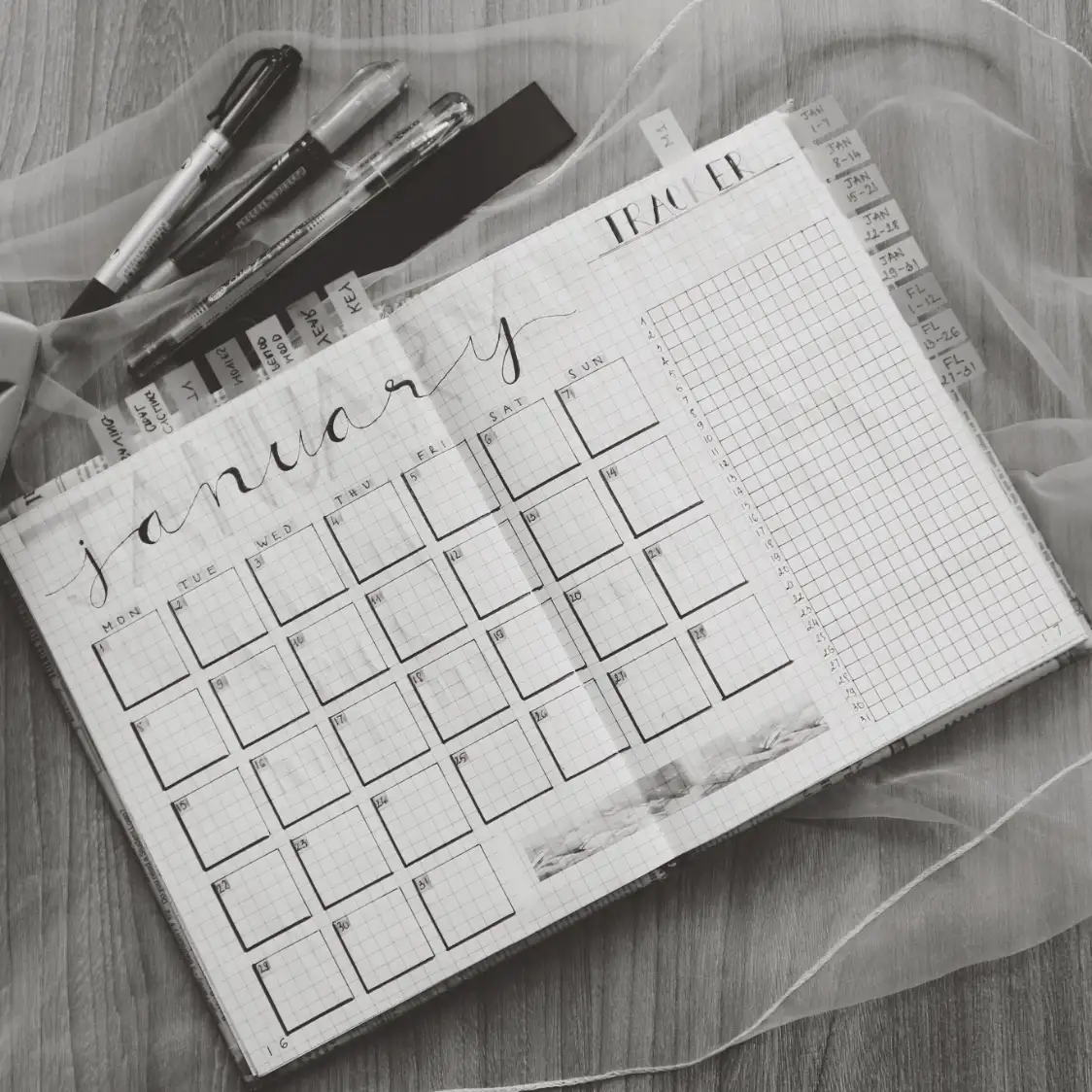 A planner open to a hand-lettered January grid, with pens and tabs