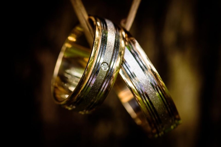 Two wedding bands hanging on a ribbon, gold edges around a textured white gold centre, one with a small diamond set flush