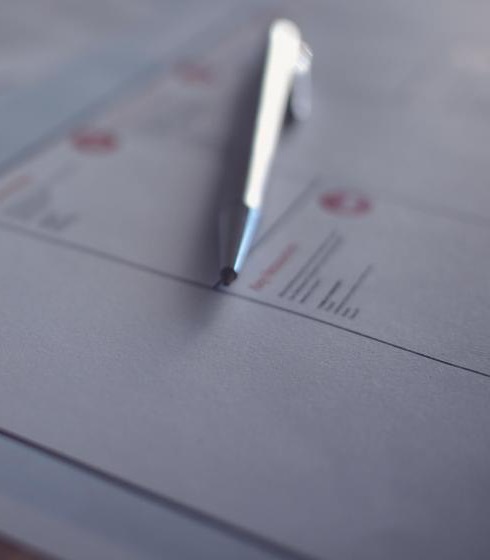 A pen resting on a printed worksheet on a desk, beside a navy notebook.