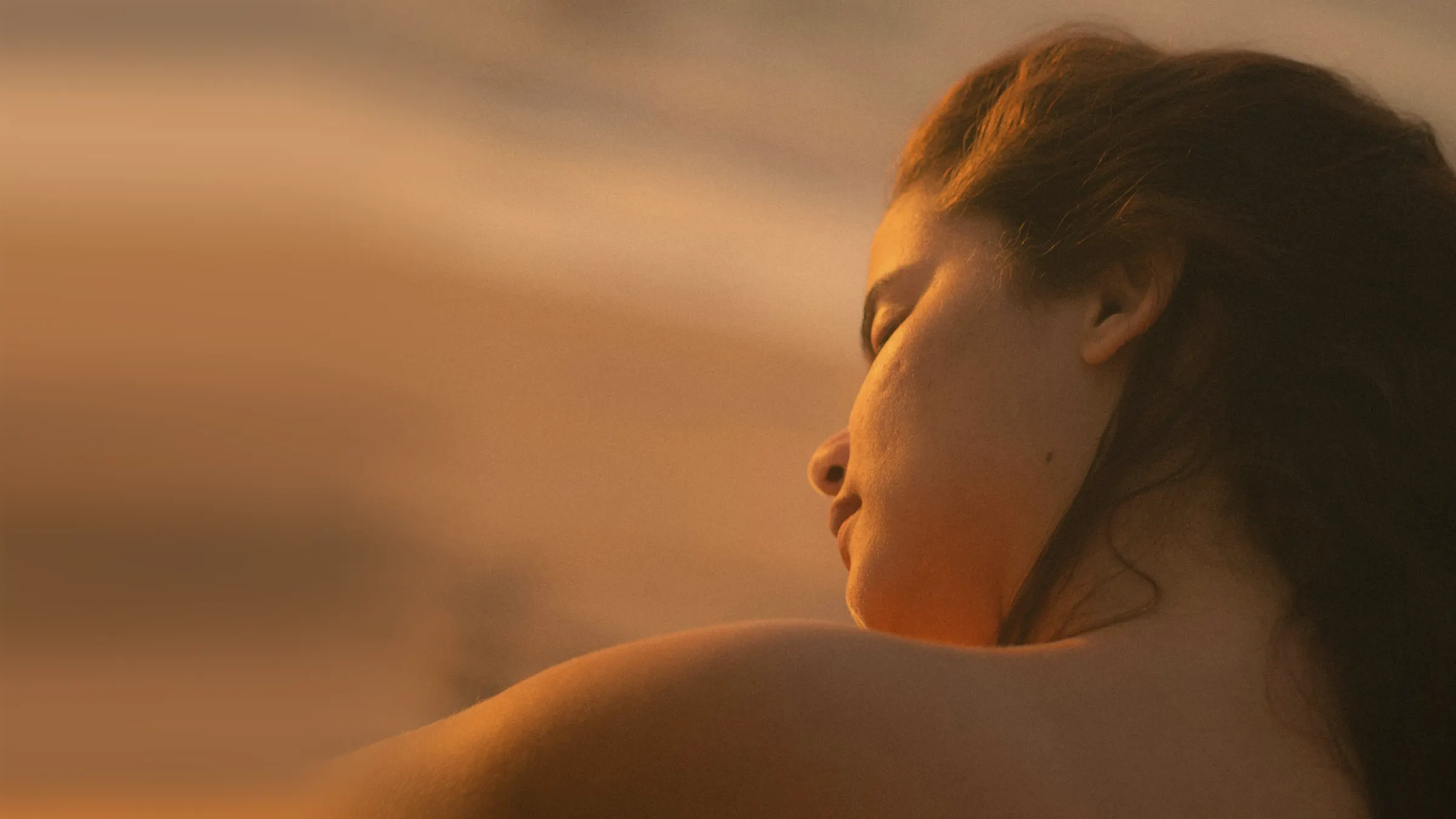A woman in warm evening sun, eyes closed and shoulders relaxed, her face turned up to the light