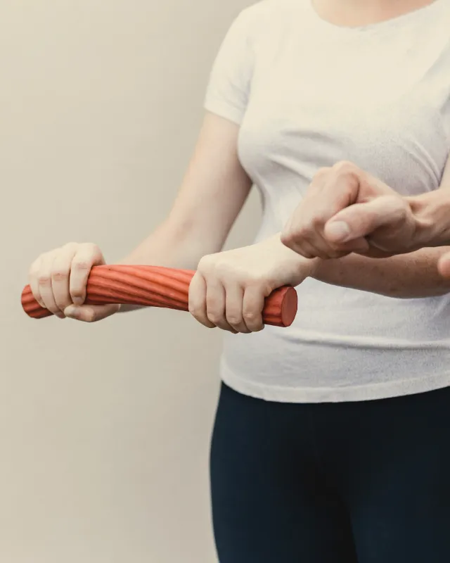 A physical therapist guiding a client's wrists as she twists a red rubber exercise bar