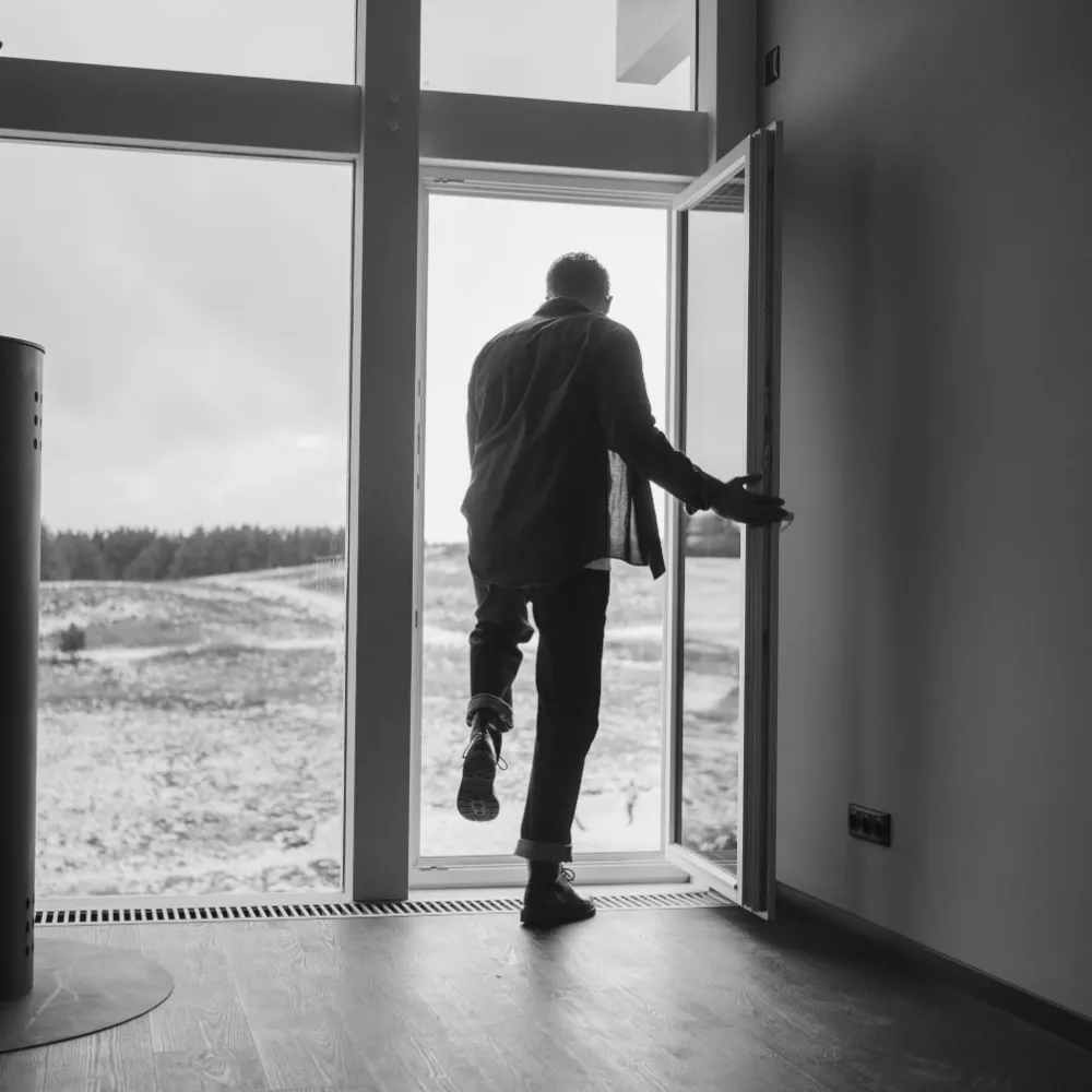 A man in a jacket stepping out through an open glass door