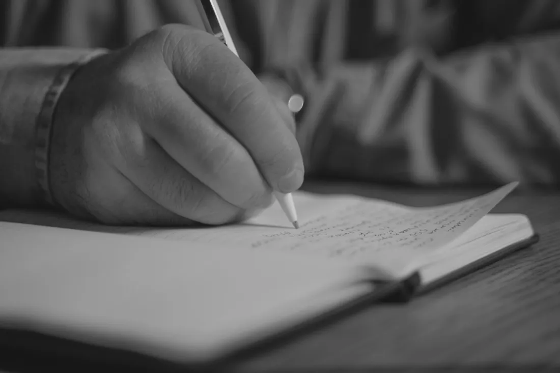 A hand holding a pen over pages of handwritten notes
