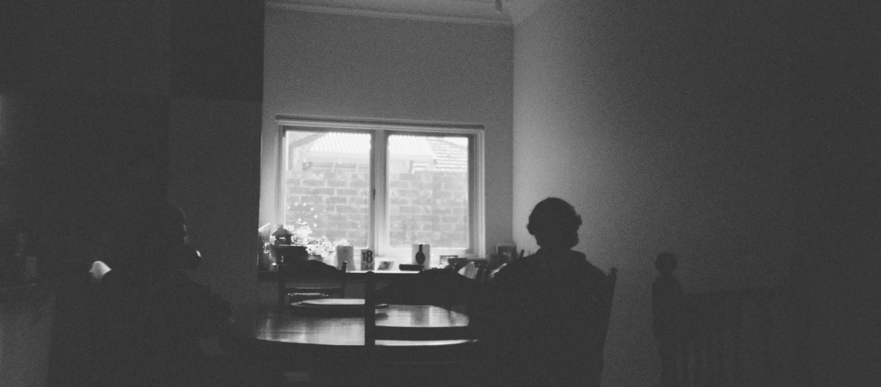 A quiet meeting room in shadow, a window glowing behind a round table