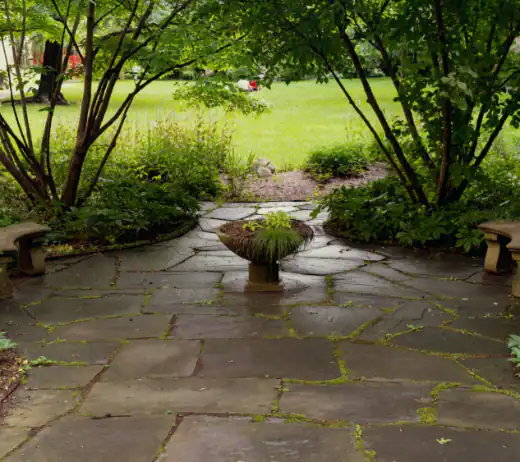 Flagstone patio with a stone planter, framed by Japanese maples and a lawn