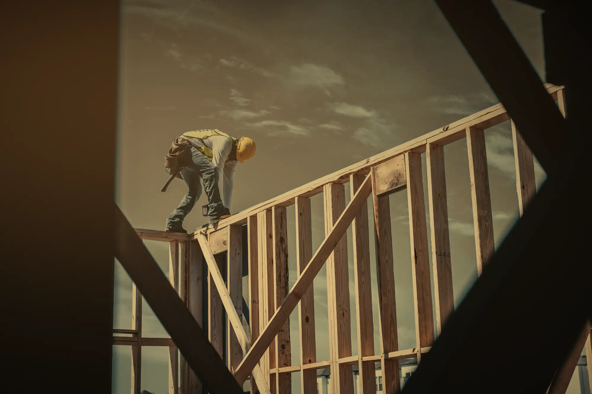A framer in a hard hat works along the top plate of a newly raised wall.