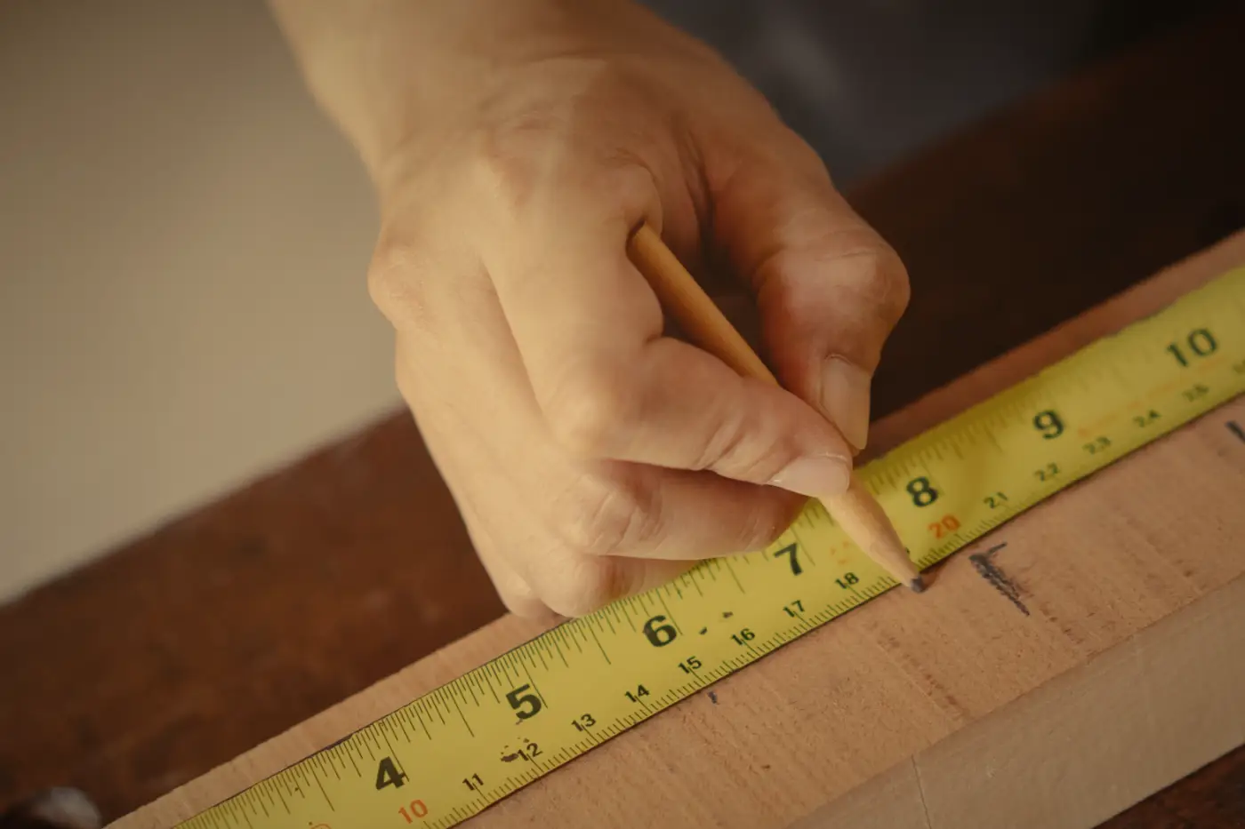 A carpenter marks a cut on a board with a pencil and a tape measure.