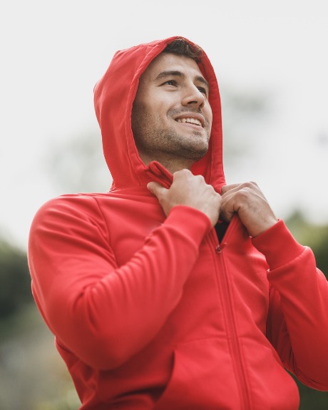 Jordan Reyes smiling, zipping up a hooded jacket outdoors
