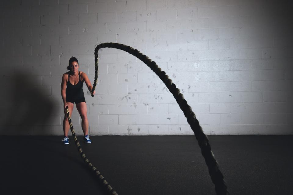 An athlete whips heavy battle ropes against a white cinderblock wall