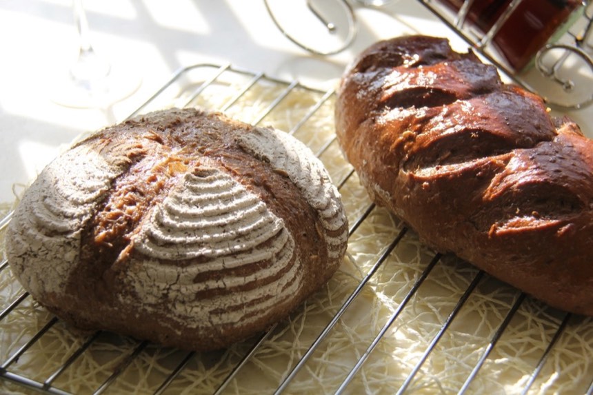 Two dark-crusted loaves cooling on a wire rack; the round one has a floured spiral pattern from its proofing basket.