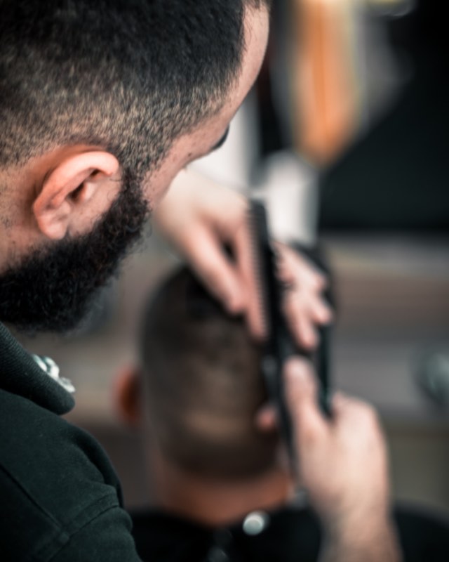 Andre, bearded, taking a client's sides down with clippers