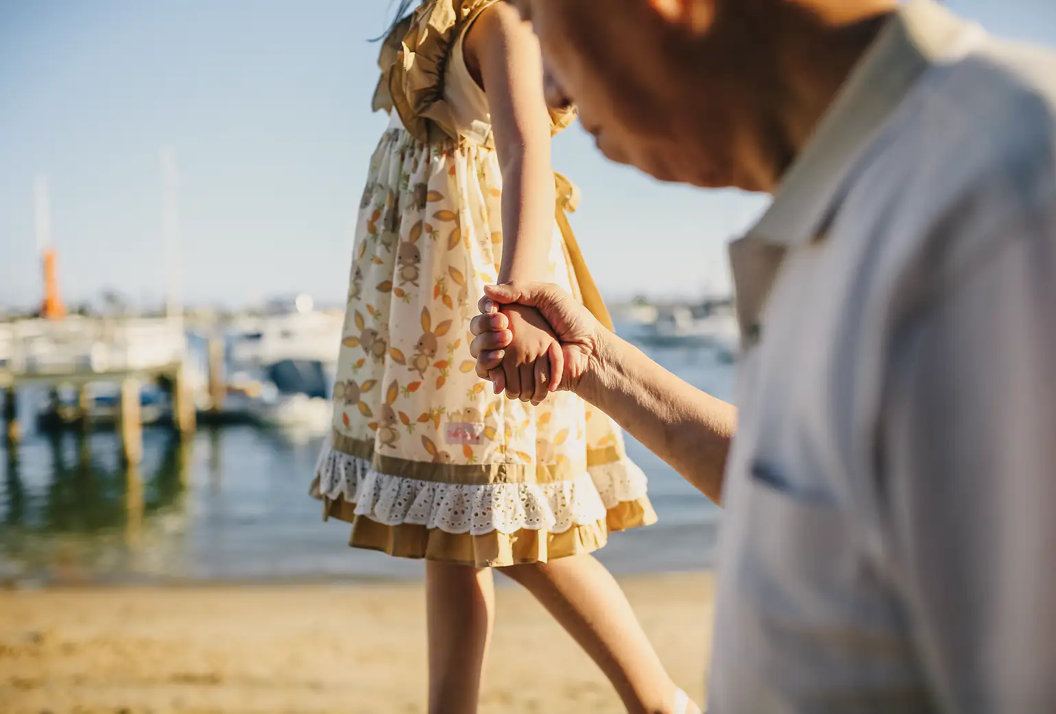 A grandfather holds his granddaughter's hand as they walk by the harbor.