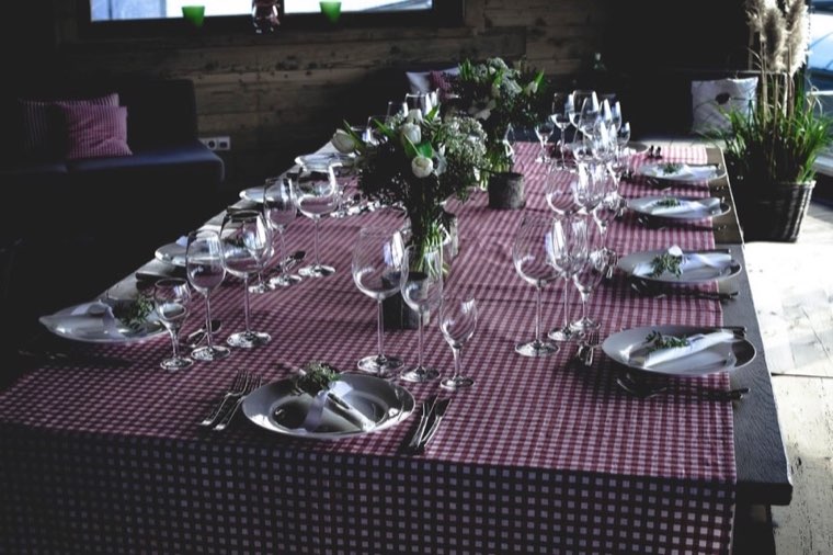 A long table set for a dinner party with a red gingham cloth, folded white napkins, wine glasses and white tulips.