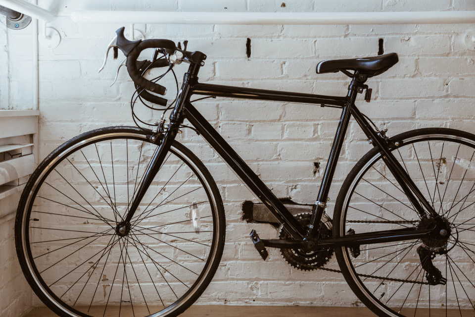 A black road bike leaning against a white painted brick wall