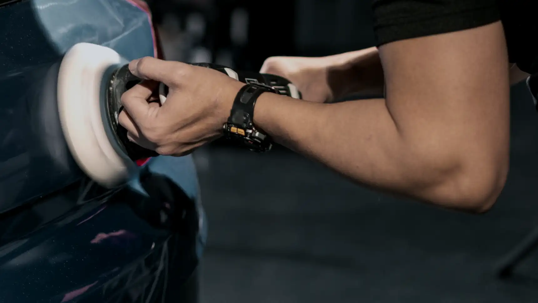 A detailer working a polisher across dark paint