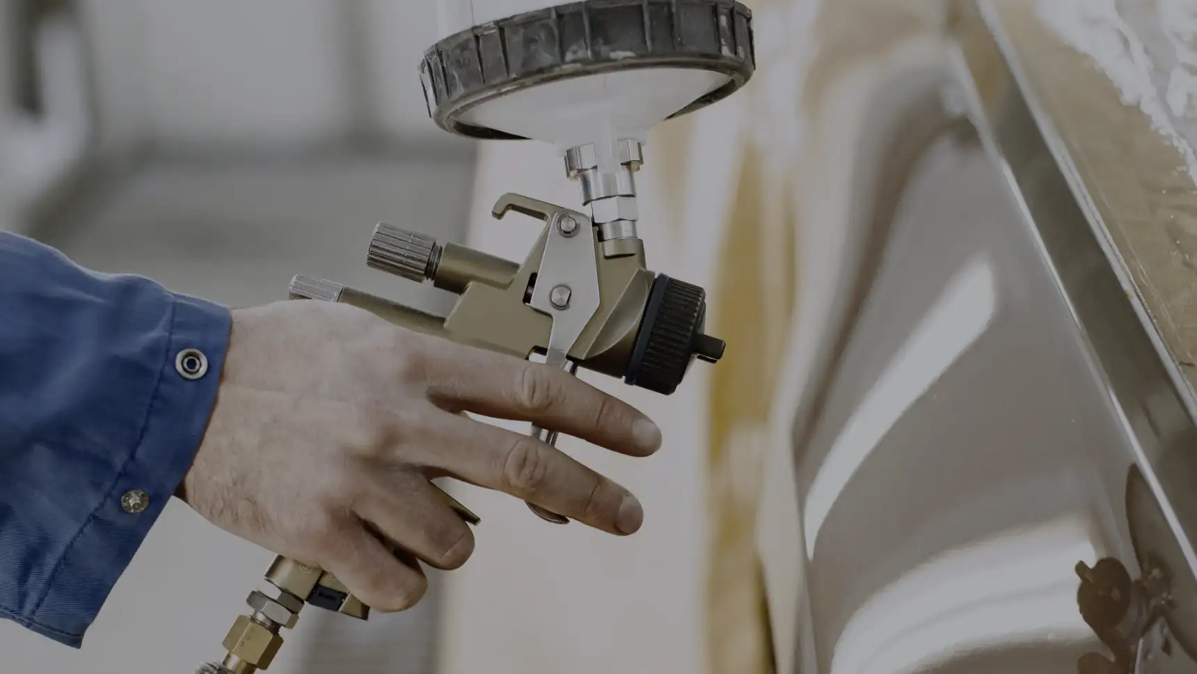 A painter's spray gun at a masked panel in the booth