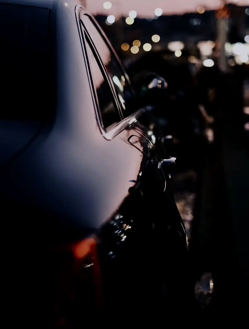 A black sedan's door and rear quarter reflecting the city at dusk
