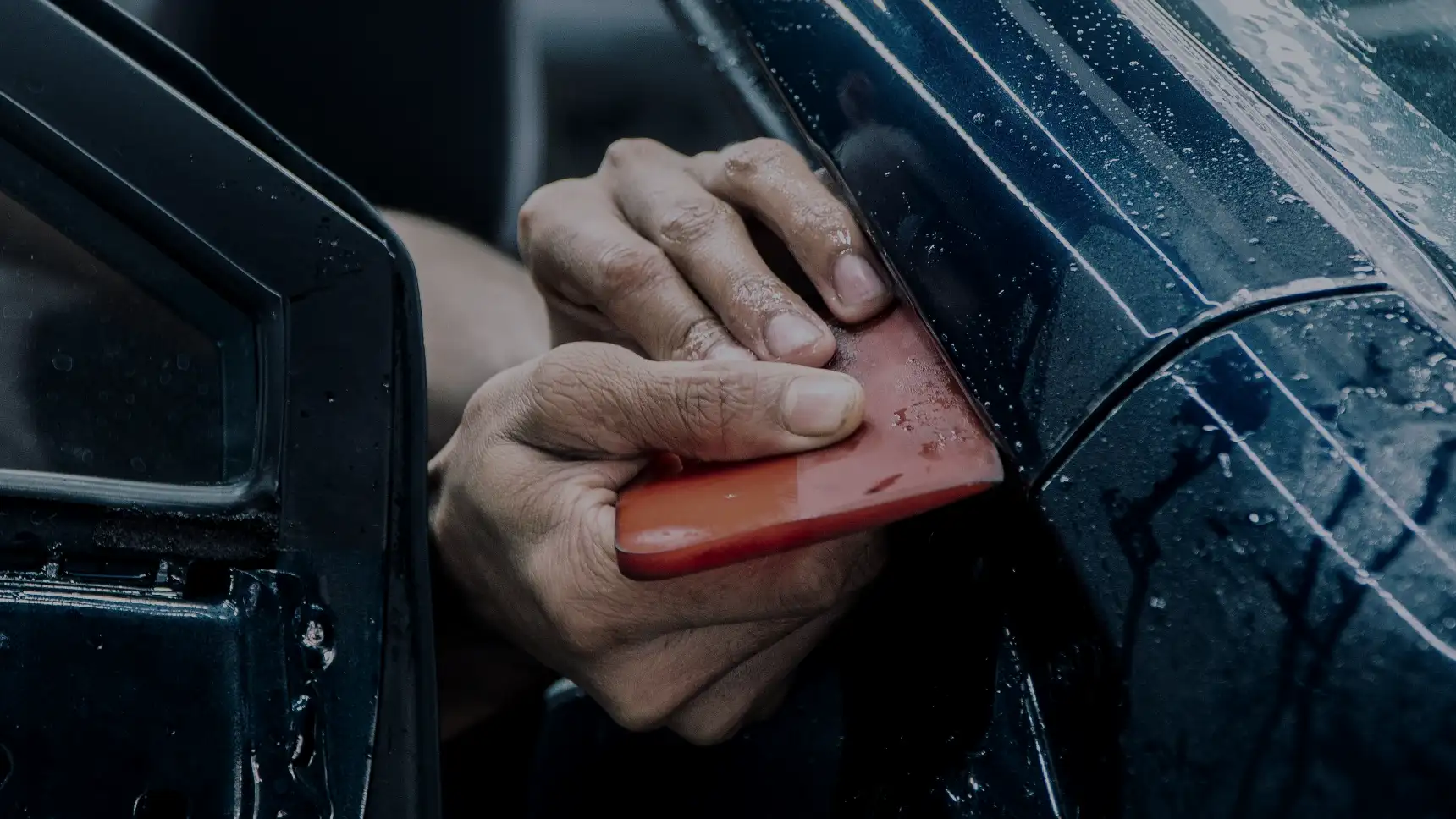 A fitter's squeegee pressing clear protection film onto a graphite car's door pillar