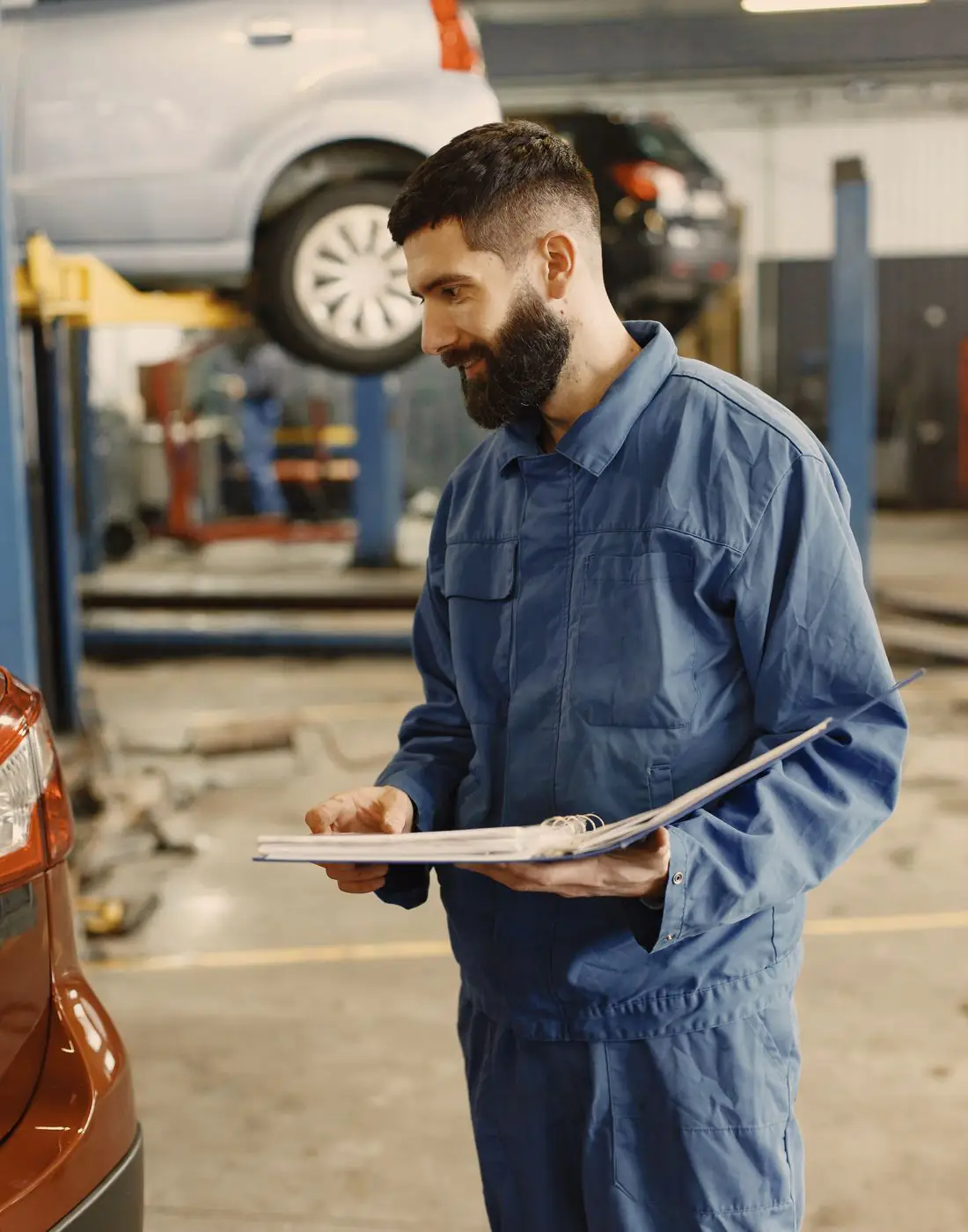 A service advisor and a mechanic go over a job sheet beside a customer's car.
