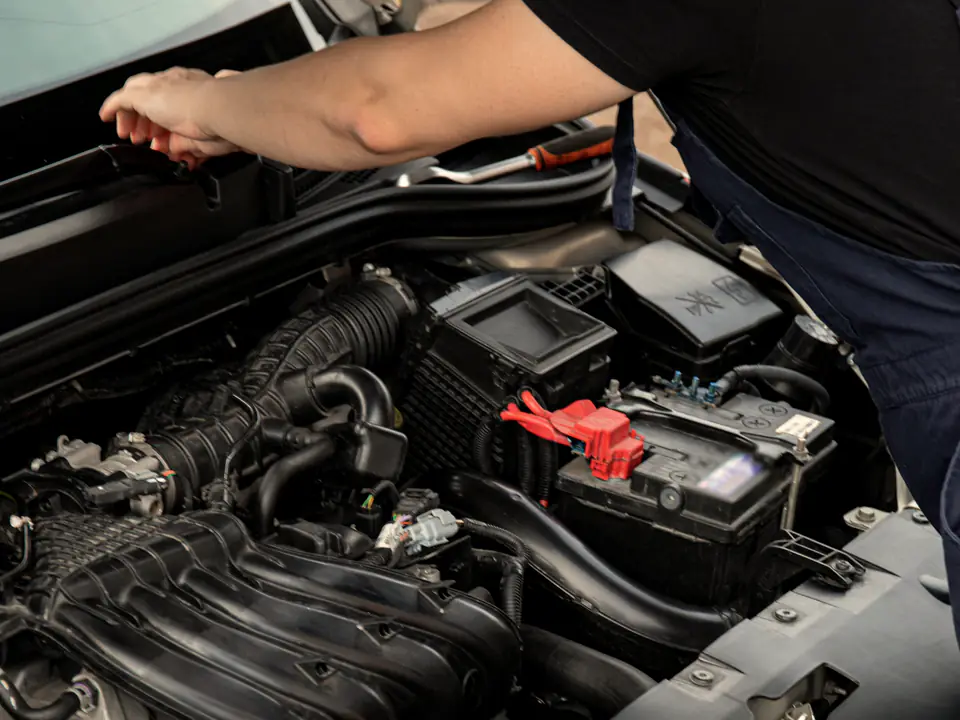 A mechanic leans into the open engine bay of a car.