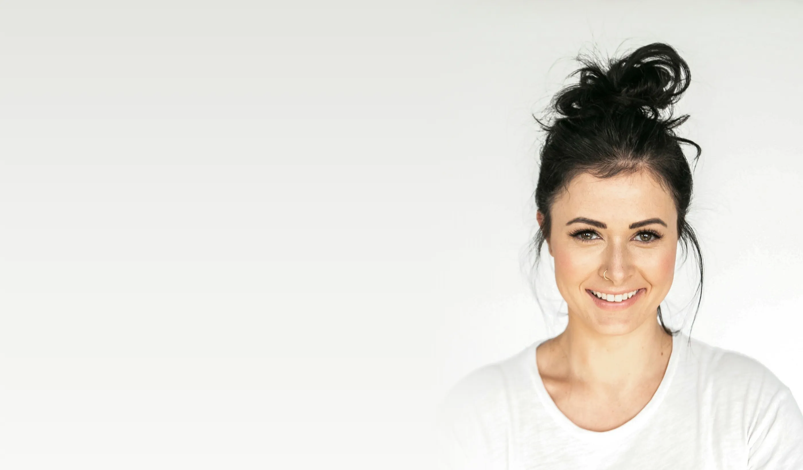 A smiling woman with her hair up in a loose bun, against a bright studio wall