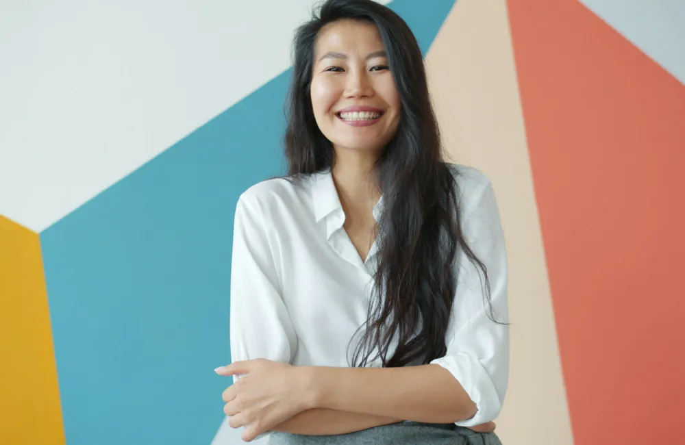 A woman in a white shirt smiling in front of a painted blue, peach and coral wall