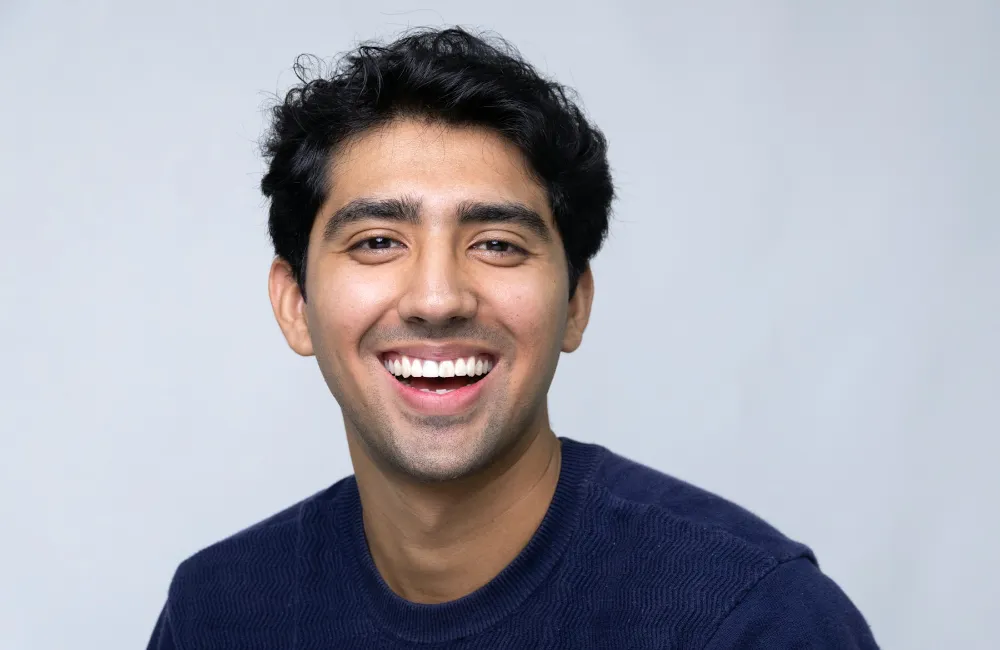 A young man in a navy sweater laughing, teeth bright and even