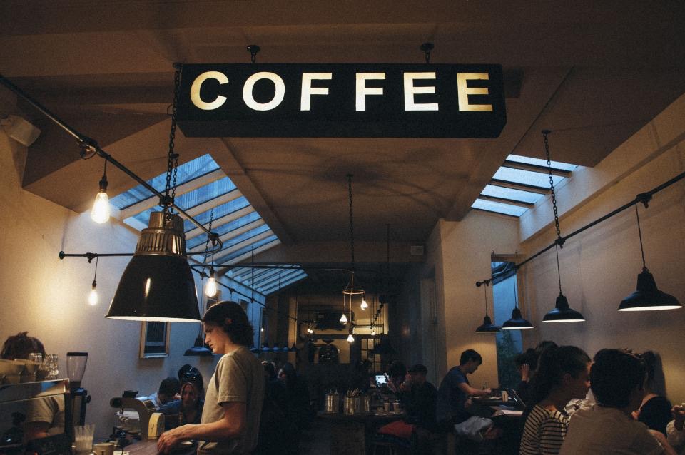 The café's long room with pendant lamps, skylights and a hanging coffee sign above the counter.