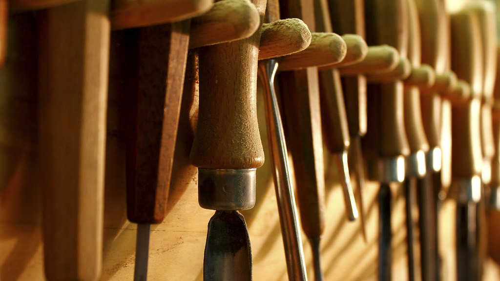 A row of carving gouges with worn wooden handles hanging on a rack in warm light
