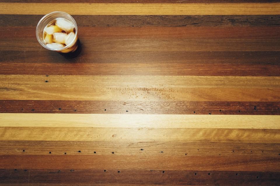 Top-down view of a table made from strips of mixed wood in light and dark tones, with old nail holes and a glass of iced coffee