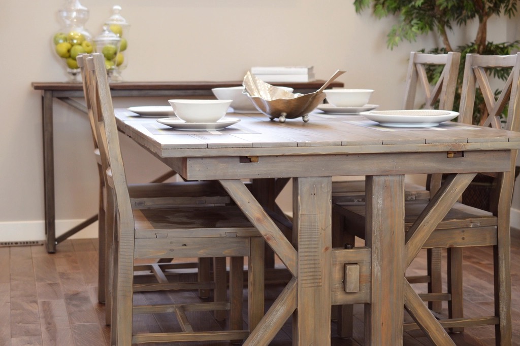 A grey-washed trestle dining table with X-shaped legs, set with white bowls and plates, and X-back chairs