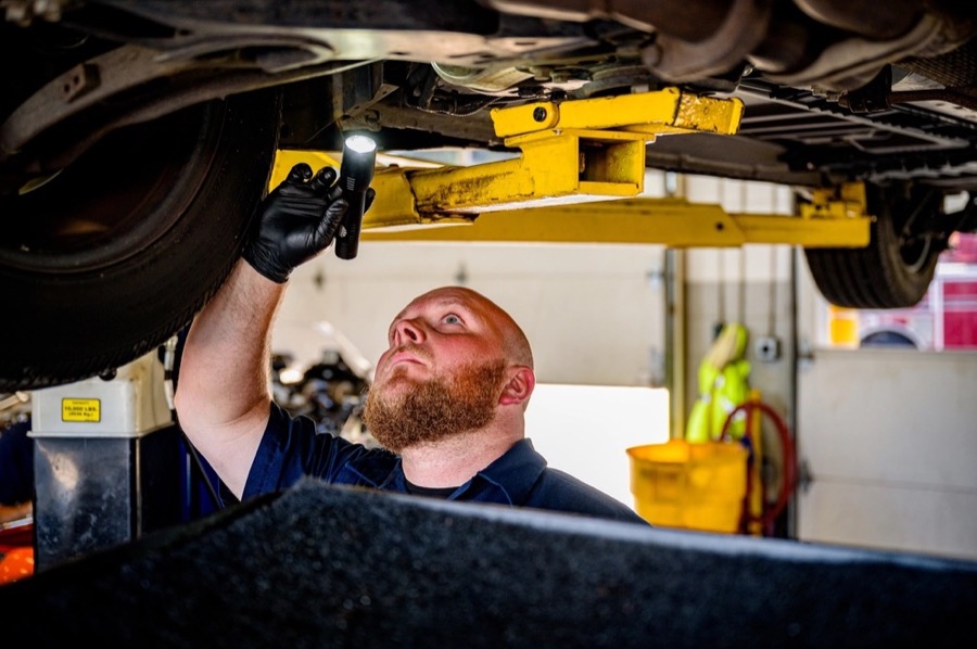 A technician checking the underside of a car on a lift with a flashlight