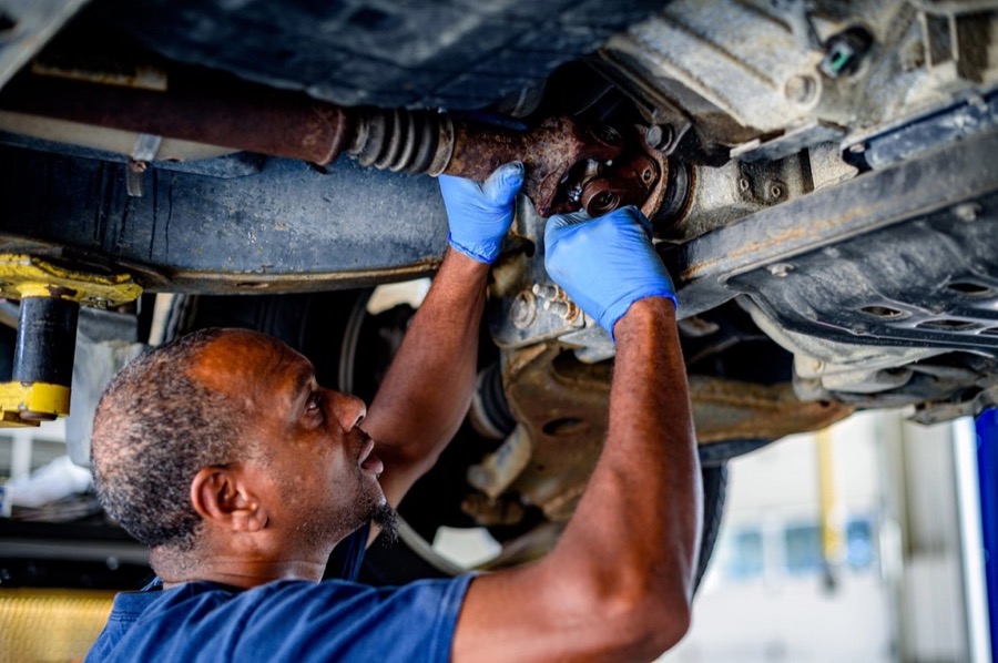 A technician in blue gloves working on a car's front suspension from below