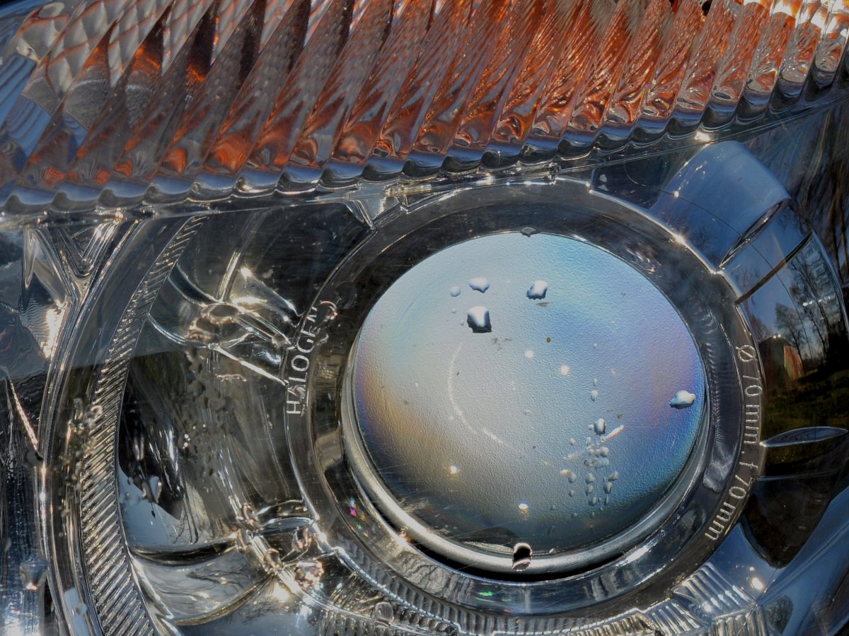 Close-up of a clear, polished headlight, with water beads over the lens and the amber indicator above