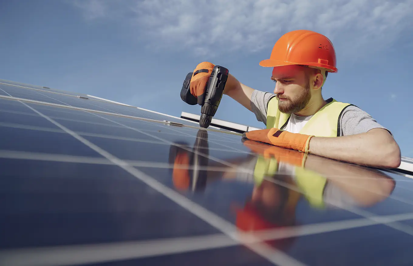 An installer in a hard hat and gloves fastens a row of rooftop solar panels.