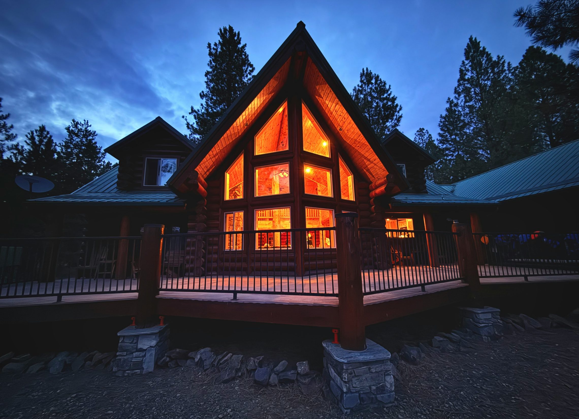 Log house at dusk with a tall glass gable, lit warmly from inside