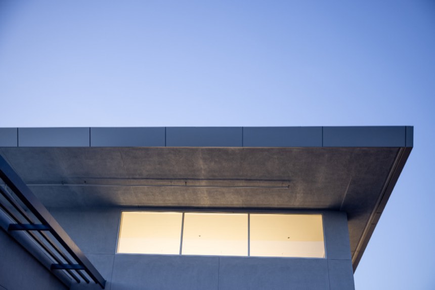 Deep flat roof overhang above a lit band of windows, against a blue evening sky