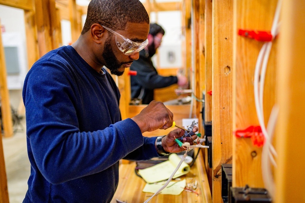 A Bluepeak technician in safety glasses wiring a new outlet box between wall studs