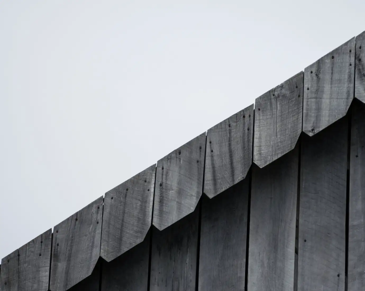 Weathered dark timber cladding along a roof edge against a pale sky
