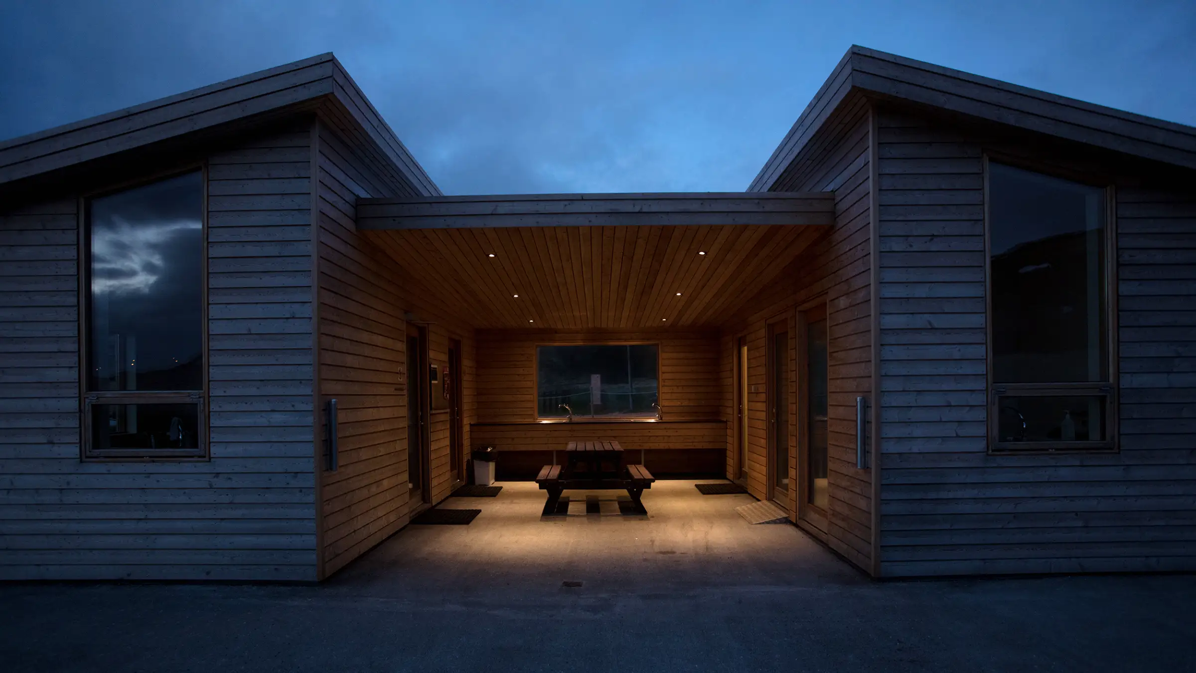 A cedar-clad house wrapped around an open courtyard, its soffit lit warm at blue hour