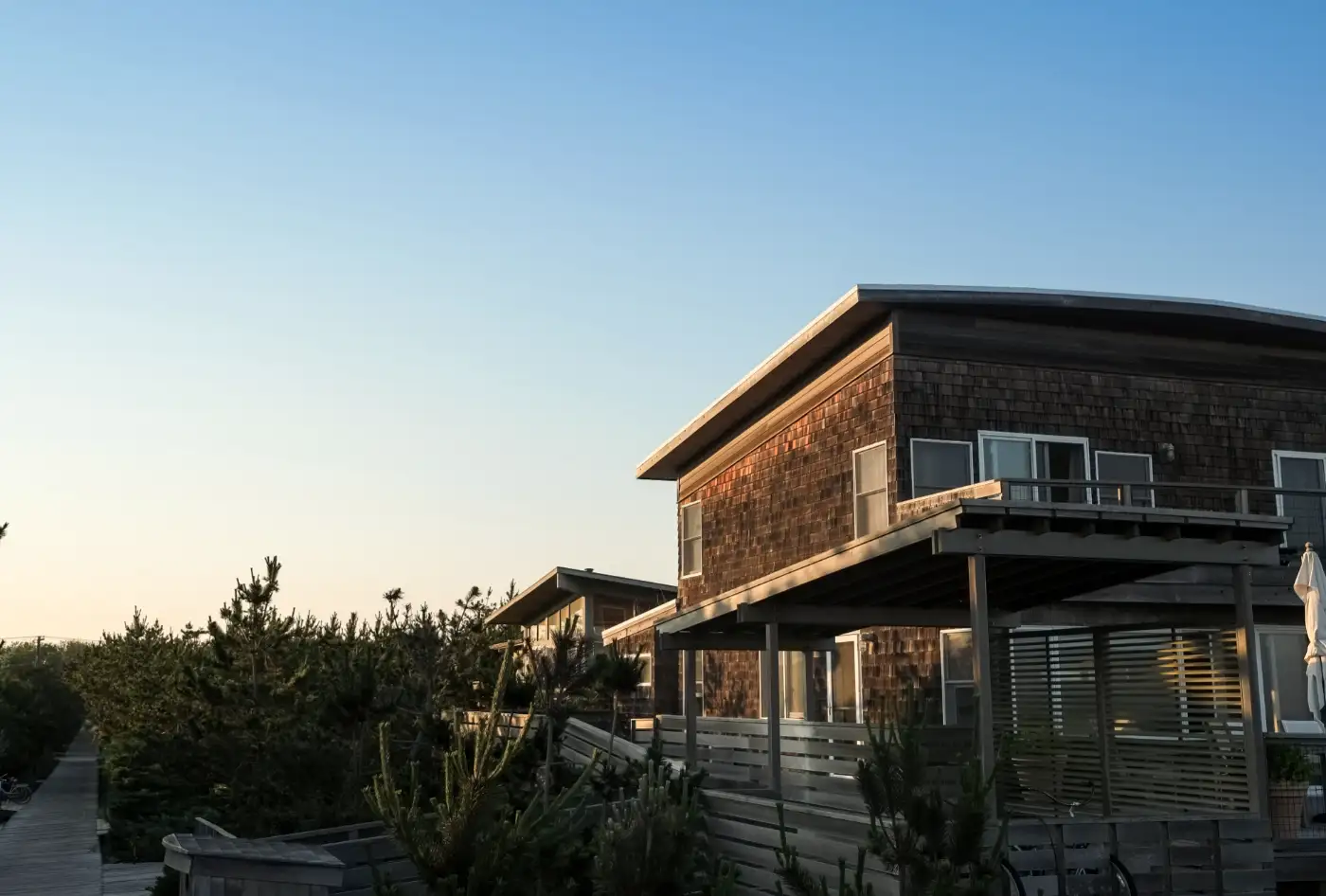 Cedar-shingled two-storey house with a deep deck among shore pines at sunset